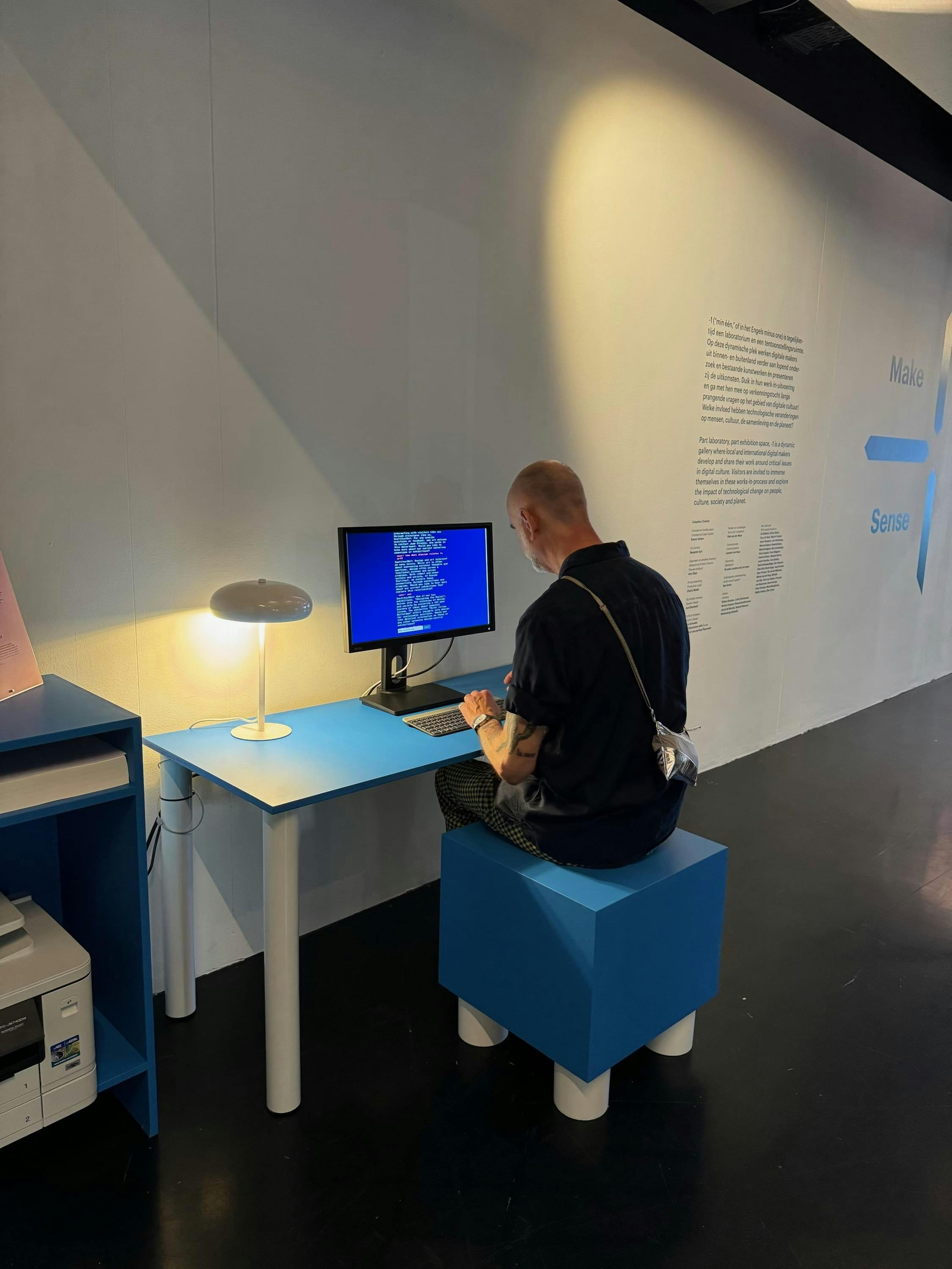 Een man in de tentoonstellingsruimte '-1' van Nieuwe Instituut die aan een tafel met computer de chatbot van Jaap Stronks gebruikt.