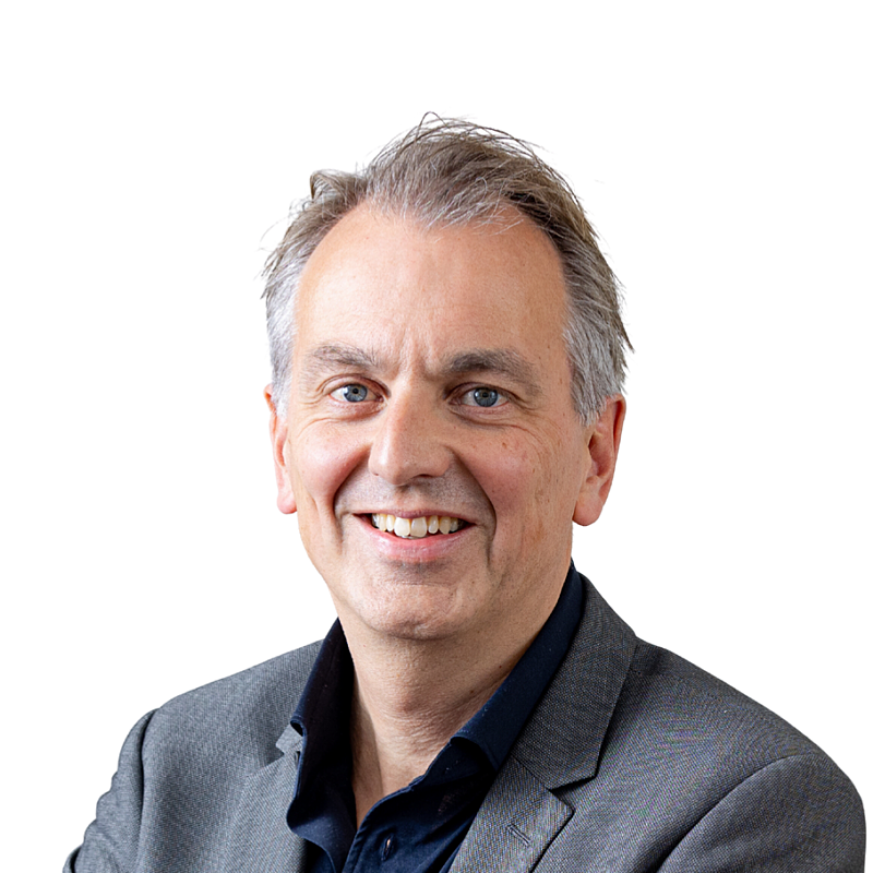 Portretfoto van Lucien Brouwer. Een man met kort grijs haar. Hij draagt een zwart overhemd en een grijs jasje.