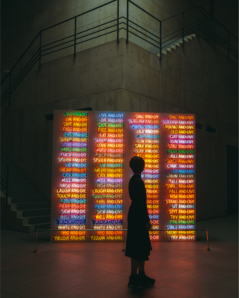 Menselijk silhouet staat voor het kunstwerk one hundred live and die, een lichtinstallatie waarbij vier rijden van 25 woordcombinaties met live of die. Bijvoorbeeld yellow and die en cry and live.